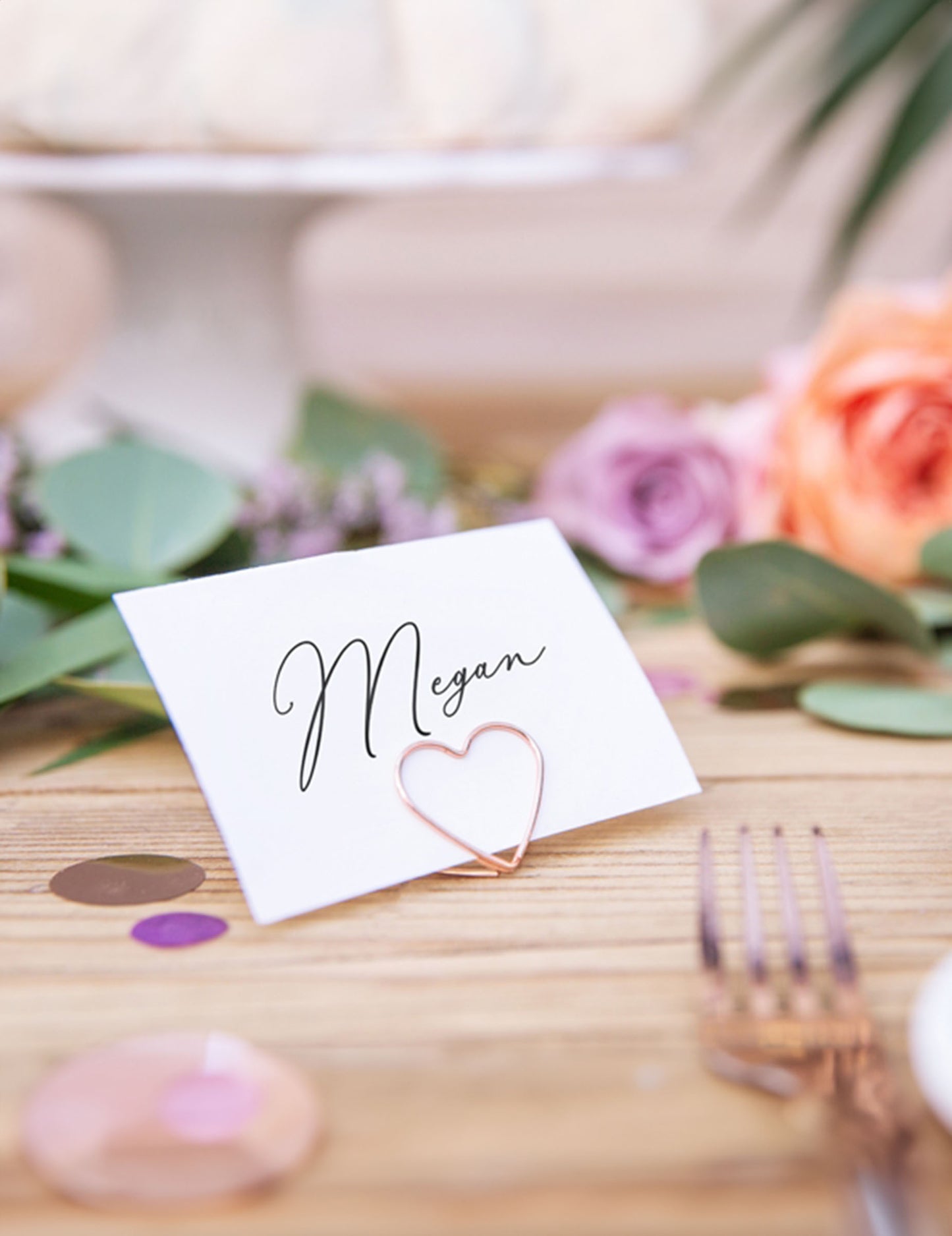 Gros plan sur une carte d'invité tenue par le marque-place cœur pour décoration de table rose gold