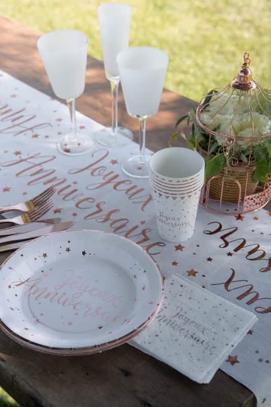 Mise en situation sur une table des serviettes en papier Joyeux Anniversaire pour fête rose gold à motifs étoiles roses