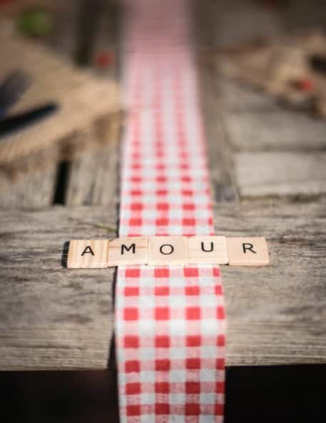 Riječ AMOUR na stolnoj traci s kariranim uzorkom iz 60 slova abecede u stilu scrabble za dekoraciju stola od drva