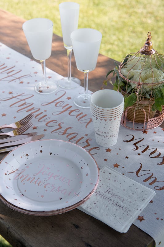 Mise en scène sur table de fête des assiettes en carton Joyeux Anniversaire blanches et rose gold à étoiles