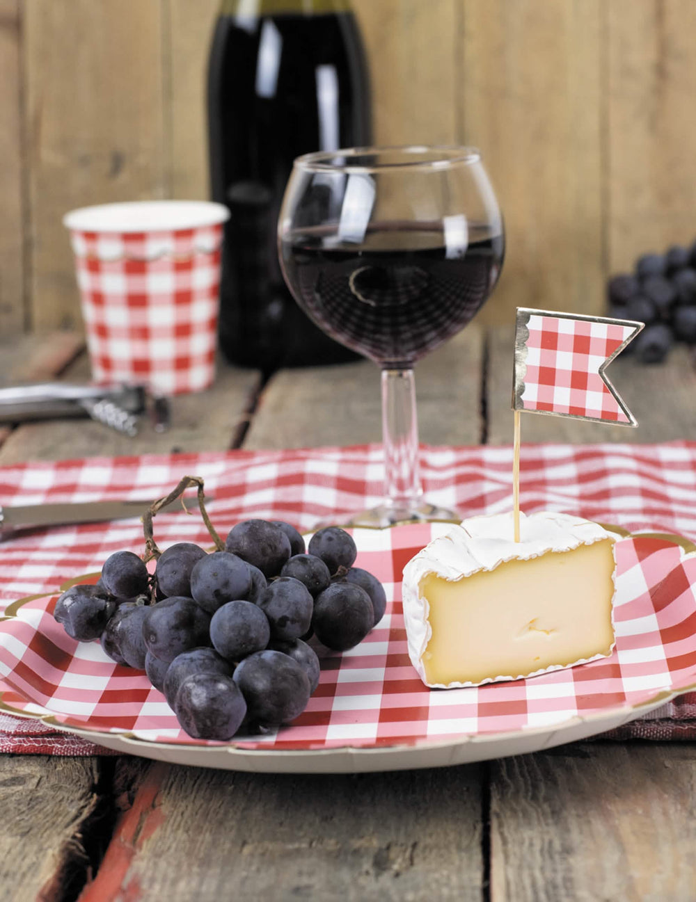 Mise en situation avec raisins et fromage des assiettes festonnées en carton vichy rouge et blanc