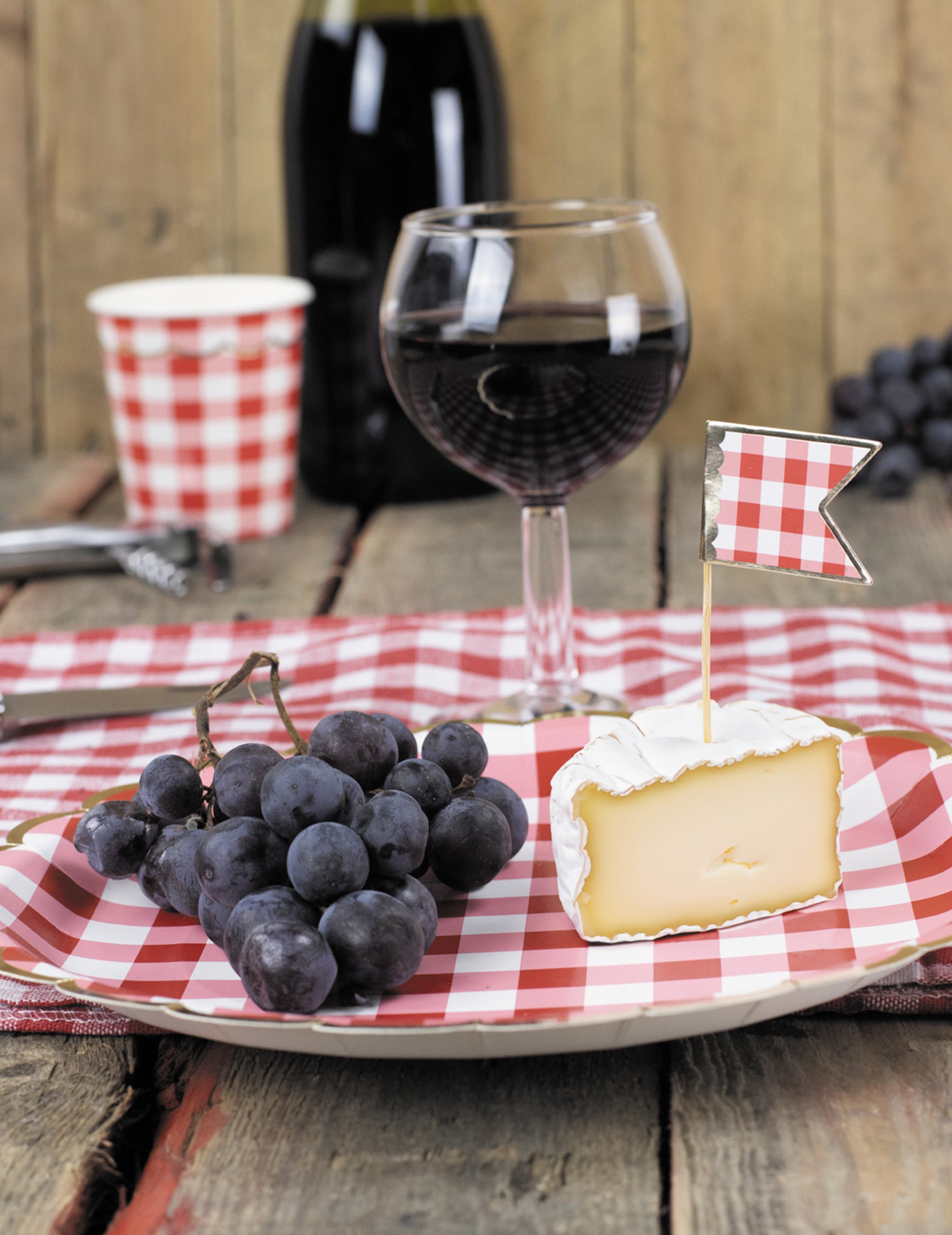Mise en situation avec raisins et fromage des assiettes festonnées en carton vichy rouge et blanc