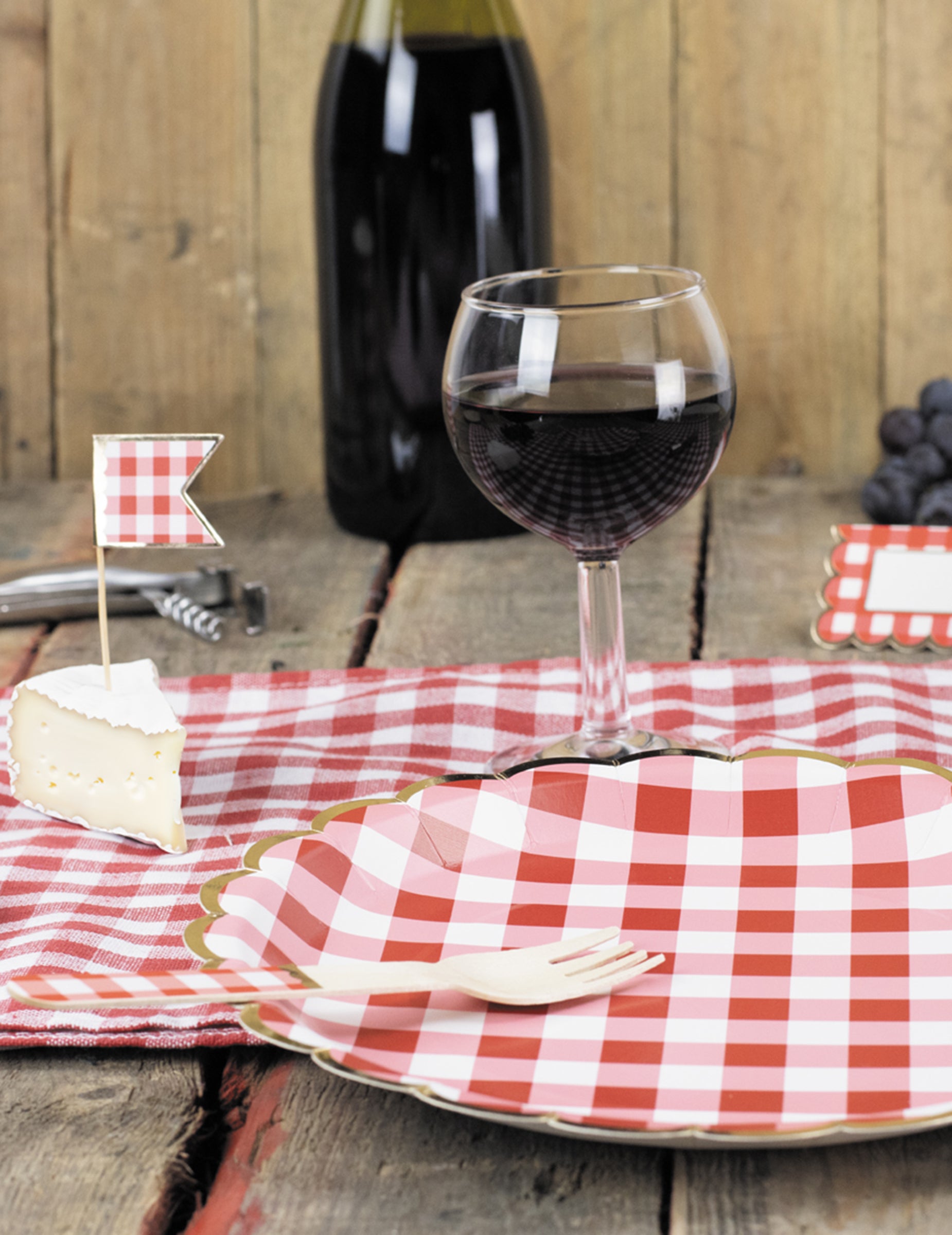 Mise en situation avec verre de vin et fourchette des assiettes festonnées en carton vichy rouge et blanc