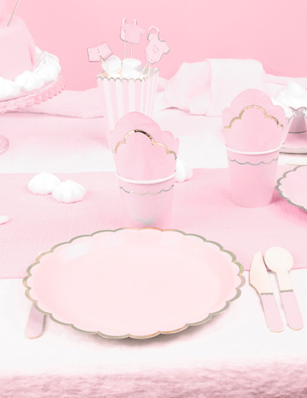 Mise en situation sur une table de fête des assiettes en carton festonnées rose pastel et or