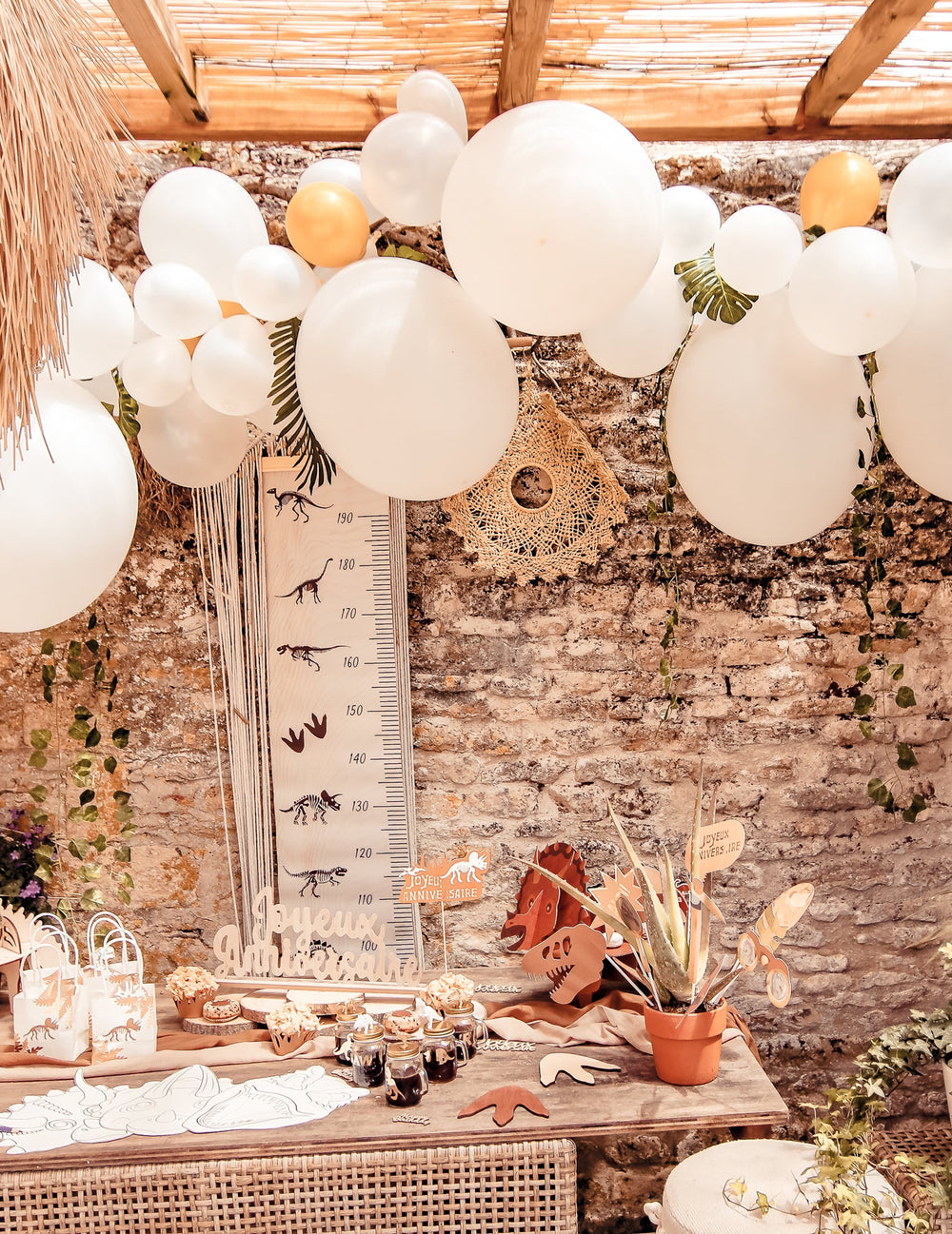 Mise en situation du kit arche de 55 ballons blanche et or avec lierre et feuilles tropicales
